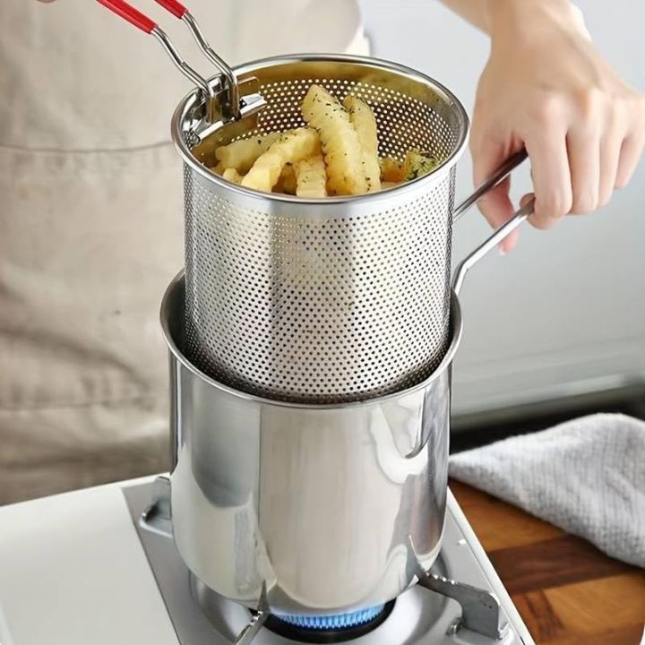 Fries being lifted from the fryer pot — perforated stainless steel strainer basket draining excess oil