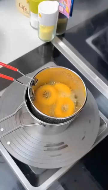 Stainless steel mini deep fryer pot in use — frying onion rings on a gas stove with the mesh strainer basket
